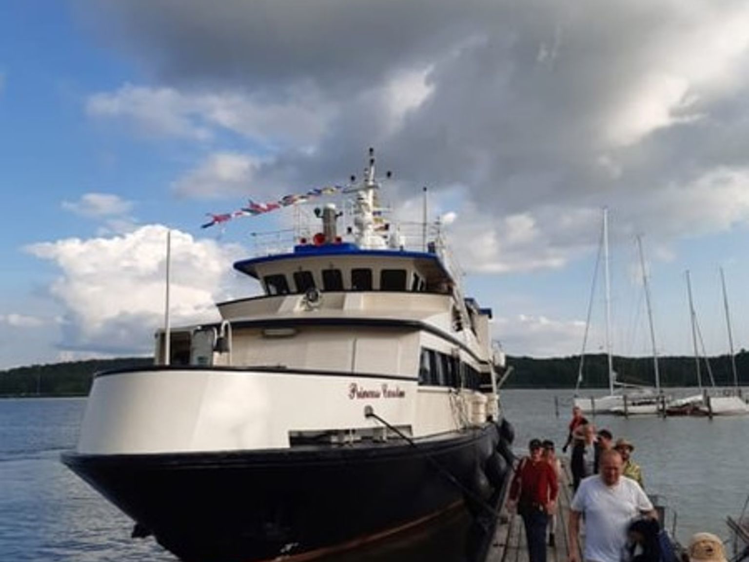 En stor båd ved navn "Princess Caroline" ligger fortøjet ved en mole, hvor folk går.