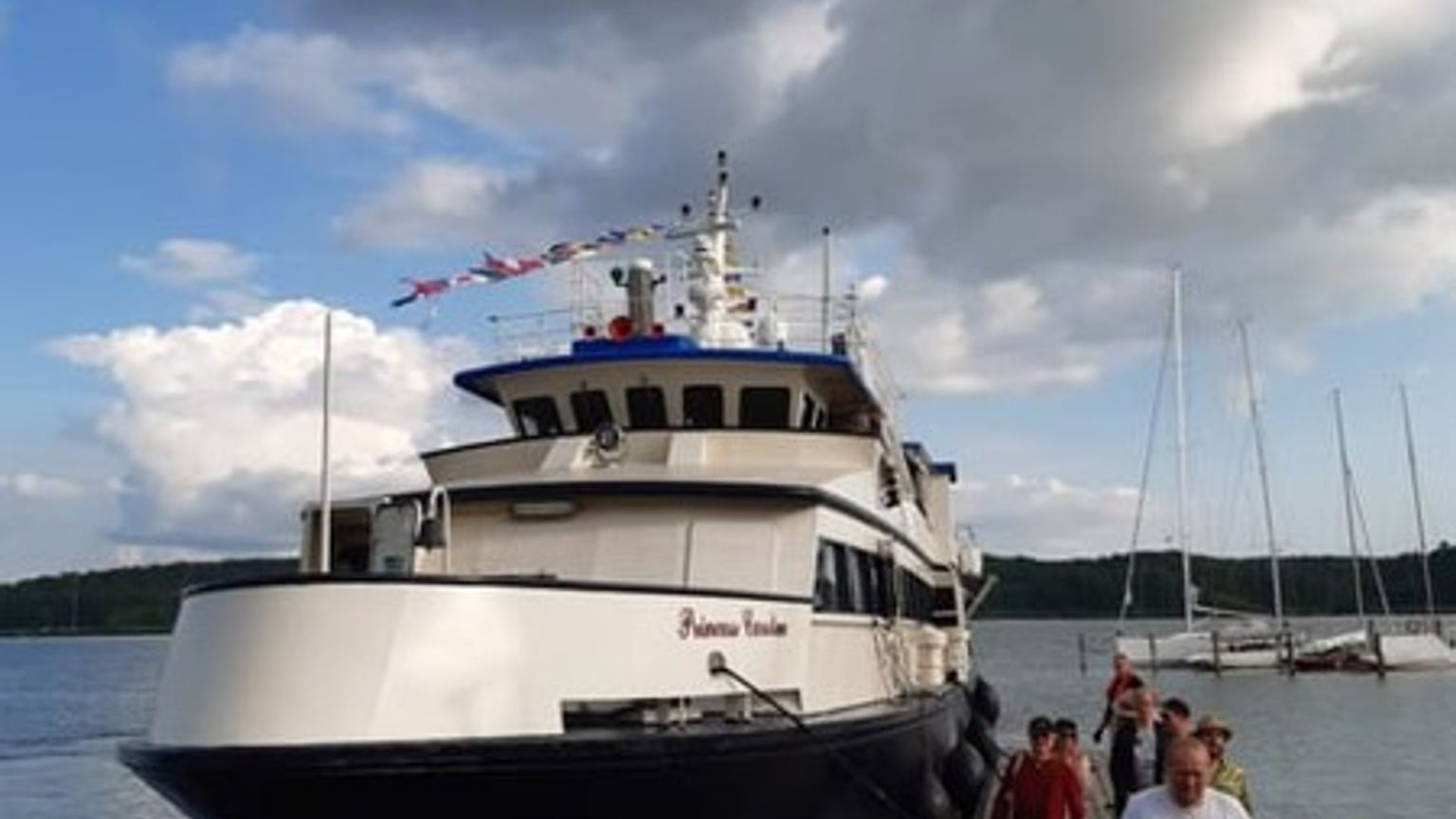 En stor båd ved navn "Princess Caroline" ligger fortøjet ved en mole, hvor folk går.