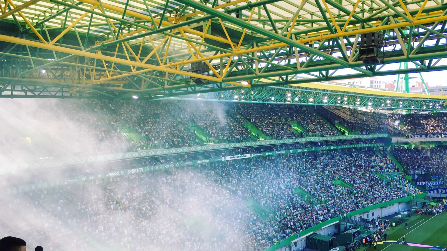 Täynnä oleva stadion, jossa on vihreä ja keltainen katto, valkoinen savu leijuu fanien täyttämien katsomoiden yllä.