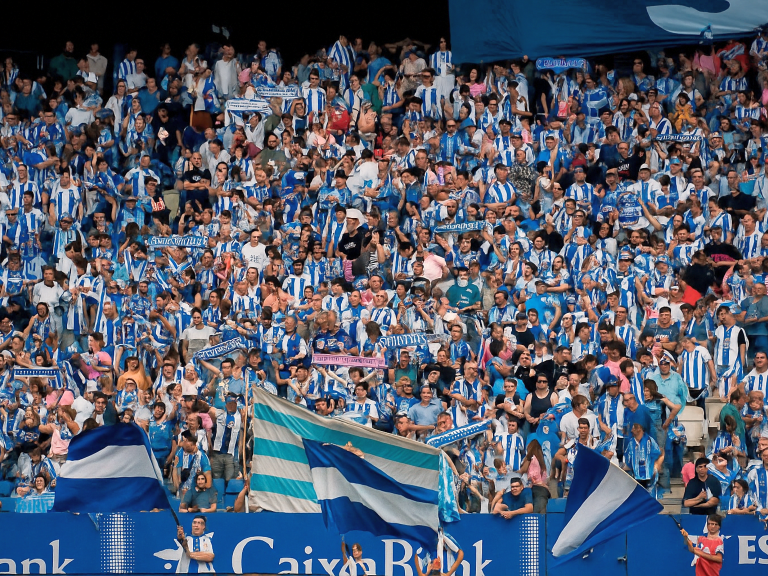 Une grande foule de fans en chemises rayées bleues et blanches remplit un stade, certains agitent des drapeaux.