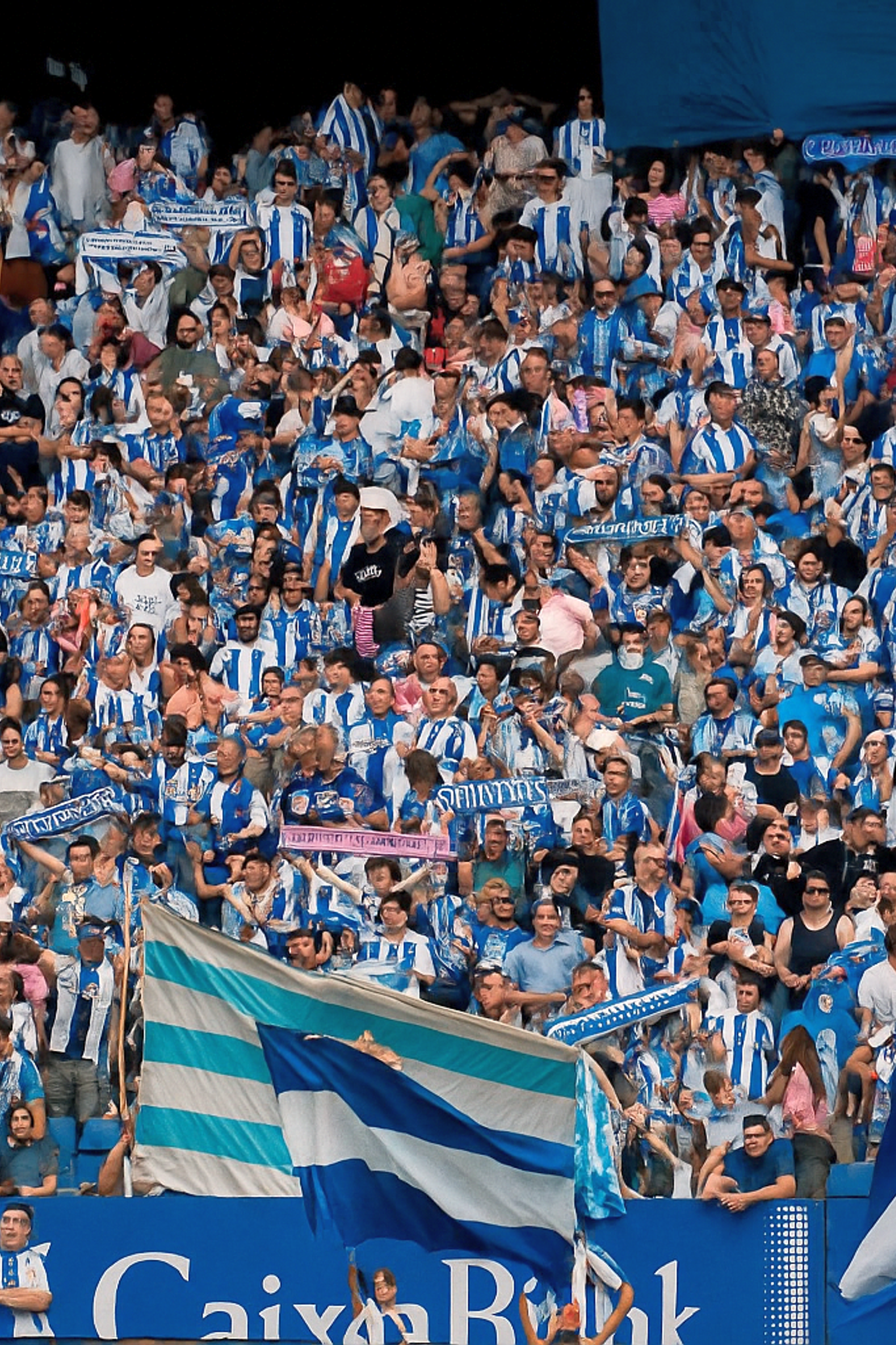 Une grande foule de fans en chemises rayées bleues et blanches remplit un stade, certains agitent des drapeaux.