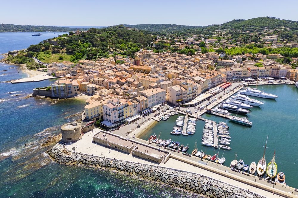 Fugleperspektiv over en travel middelhavshavn med fargerike bygninger og en rekke båter fortøyd i havnen. Saint-Tropez