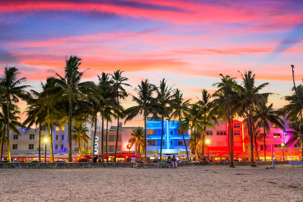 Miami Beach ved solnedgang med palmer, en sandstrand og Art Deco-bygninger oplyst af farverige neonlys. Miami, USA