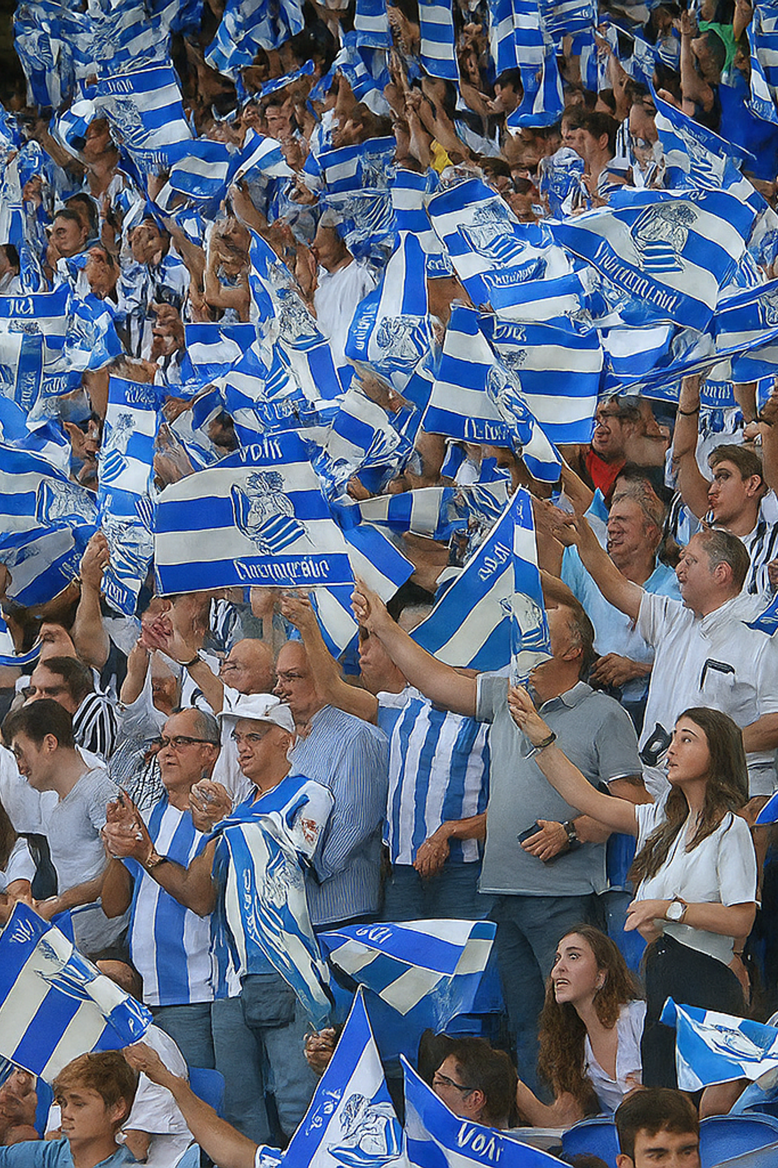 A large crowd of people waves numerous blue and white striped flags, many wearing matching attire.