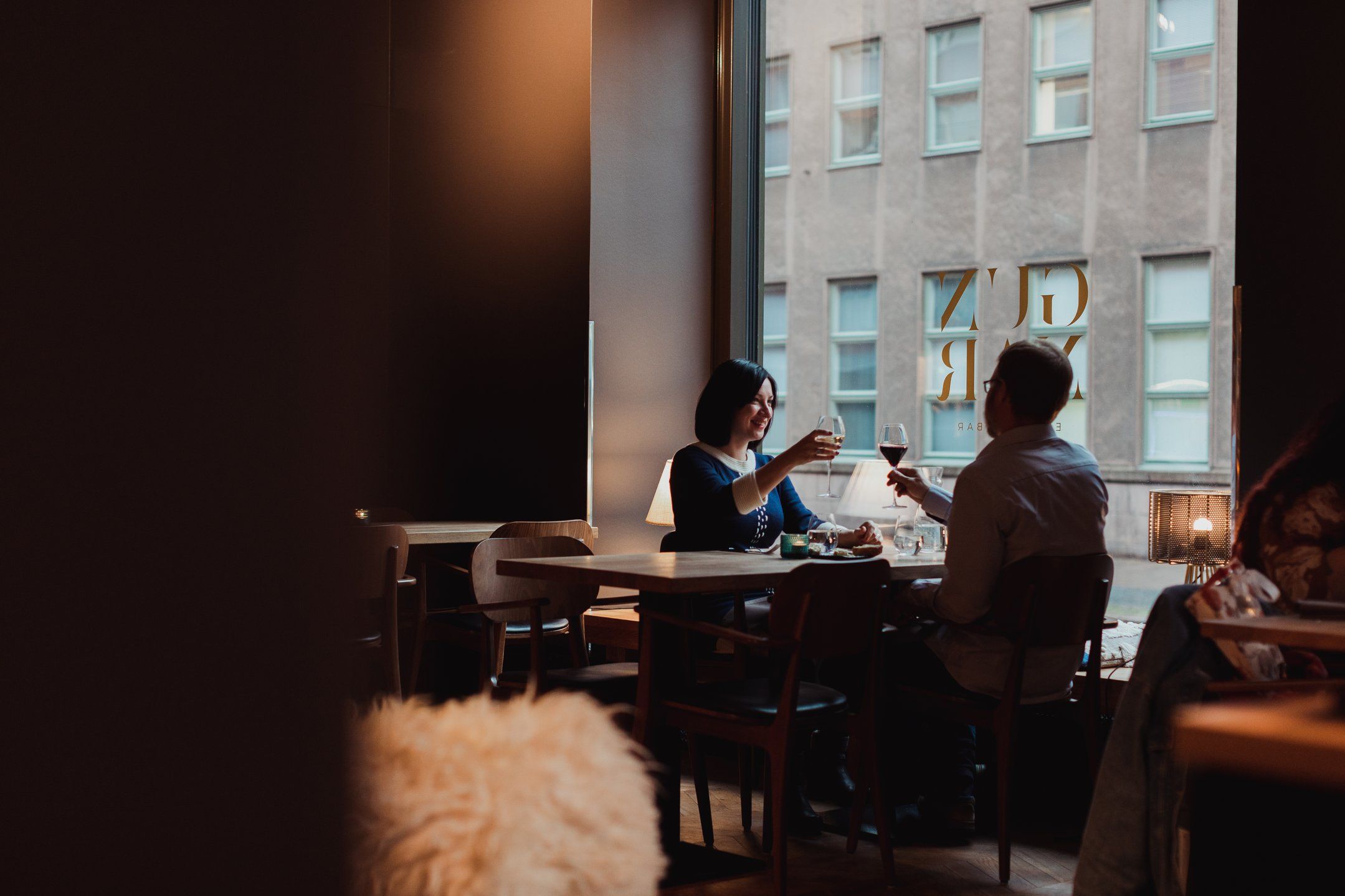 Et par skåler med vinglas ved et restaurantbord ved et stort vindue med udsigt over en bybygning.