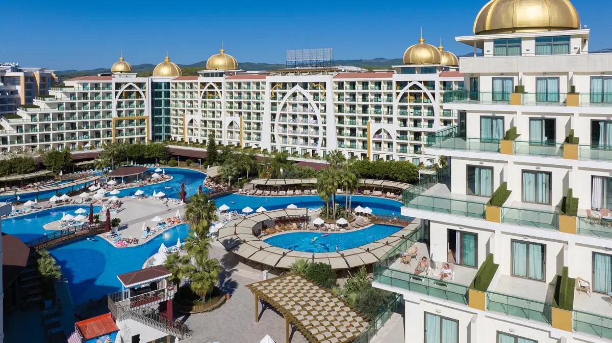 A sprawling resort complex with buildings featuring golden domes, multiple large swimming pools, and people relaxing. Alan Xafira Deluxe Resort & Spa, Alanya