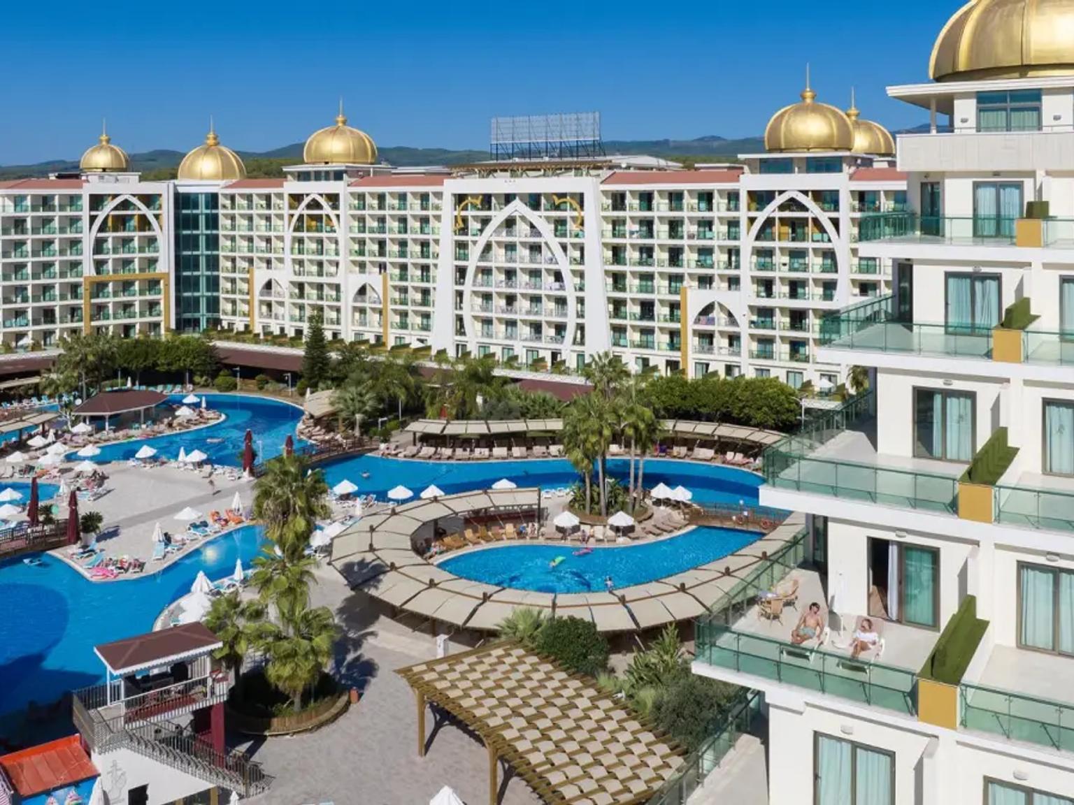Ett vidsträckt resortkomplex med byggnader som har gyllene kupoler, flera stora swimmingpooler och människor som kopplar av. Alan Xafira Deluxe Resort & Spa, Alanya