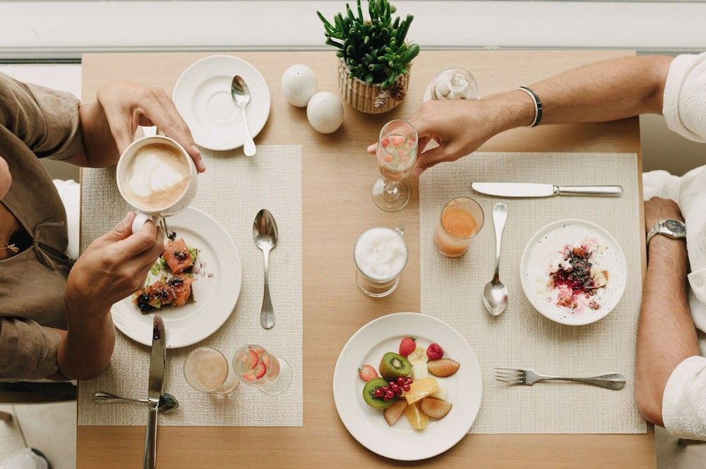 Draufsicht auf zwei Personen, die ein Frühstücksbuffet mit Kaffee, Obst und verschiedenen Gerichten genießen. Iberostar Selection Llaut Palma – Nur für Erwachsene