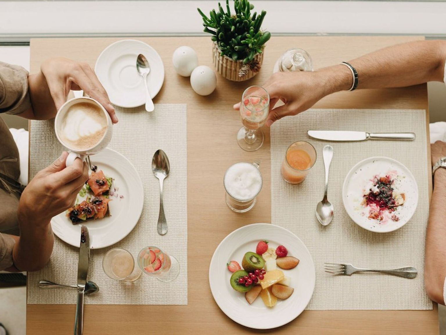 Draufsicht auf zwei Personen, die ein Frühstücksbuffet mit Kaffee, Obst und verschiedenen Gerichten genießen. Iberostar Selection Llaut Palma – Nur für Erwachsene