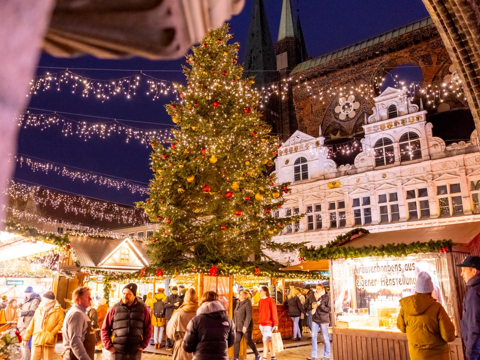 en grupp människor går runt en julmarknad med ett julgran i bakgrunden