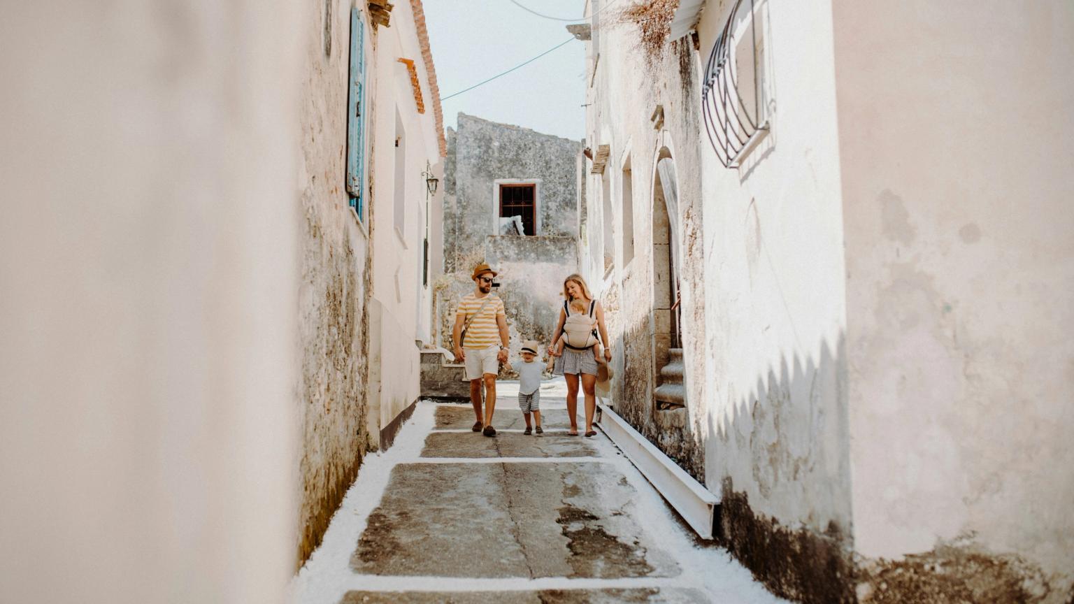 En familie med et lille barn går ned ad en smal, trappet gade flankeret af hvidkalkede bygninger.