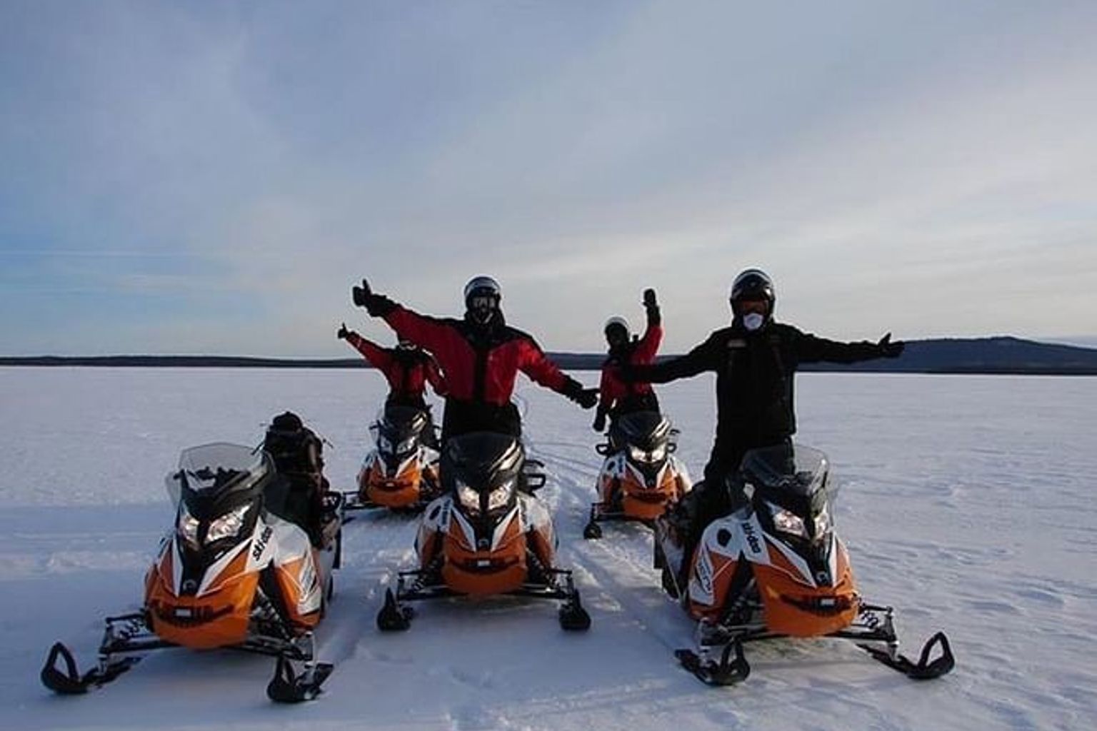 eine Gruppe von Menschen steht nebeneinander auf Schneemobilen im Schnee