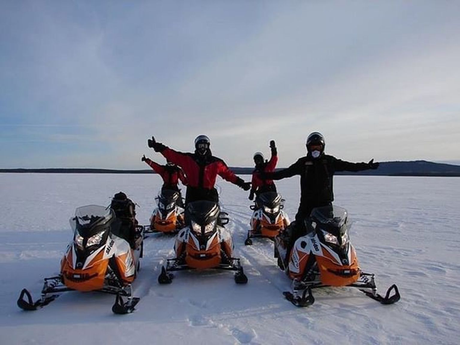 un grupo de personas están paradas una al lado de la otra en motos de nieve en la nieve