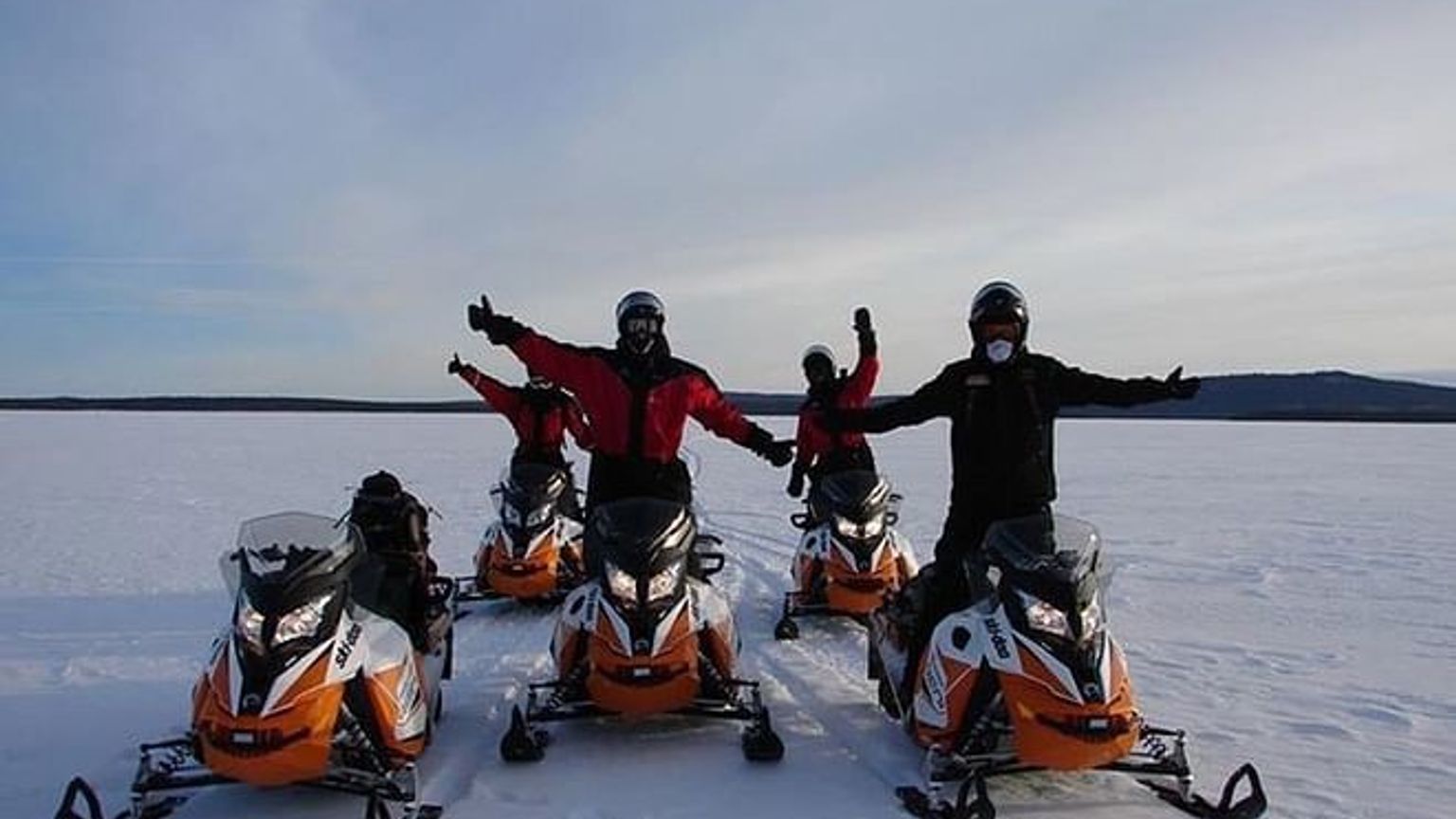 eine Gruppe von Menschen steht nebeneinander auf Schneemobilen im Schnee