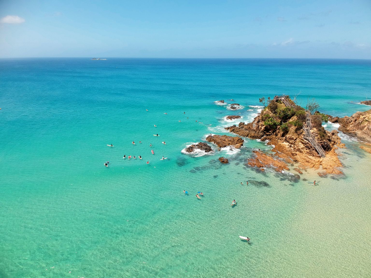 a group of people are swimming in the ocean near a rocky shoreline
