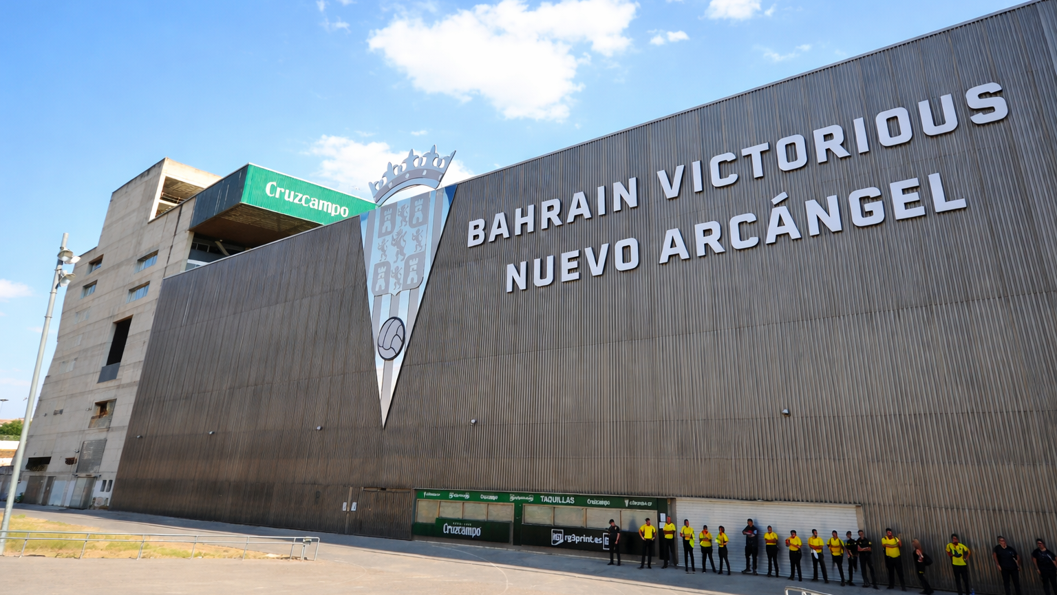 Exterior of the Nuevo Arcángel stadium with the text "Bahrain Victorious" and a crest, with people standing below.