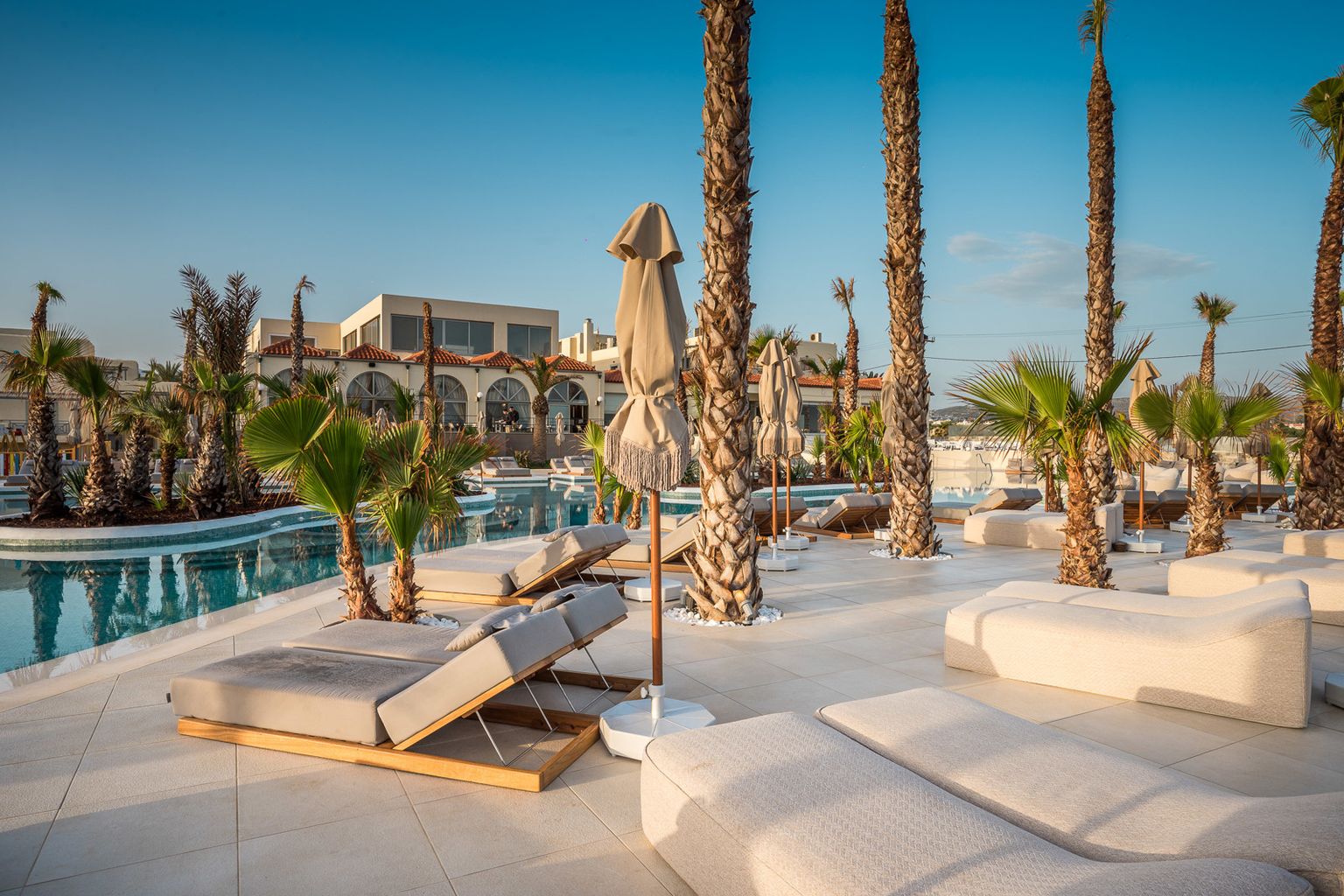 Zona de piscina soleada en un resort con palmeras, tumbonas modernas y edificios del hotel. Stella Blue Seaside Resort