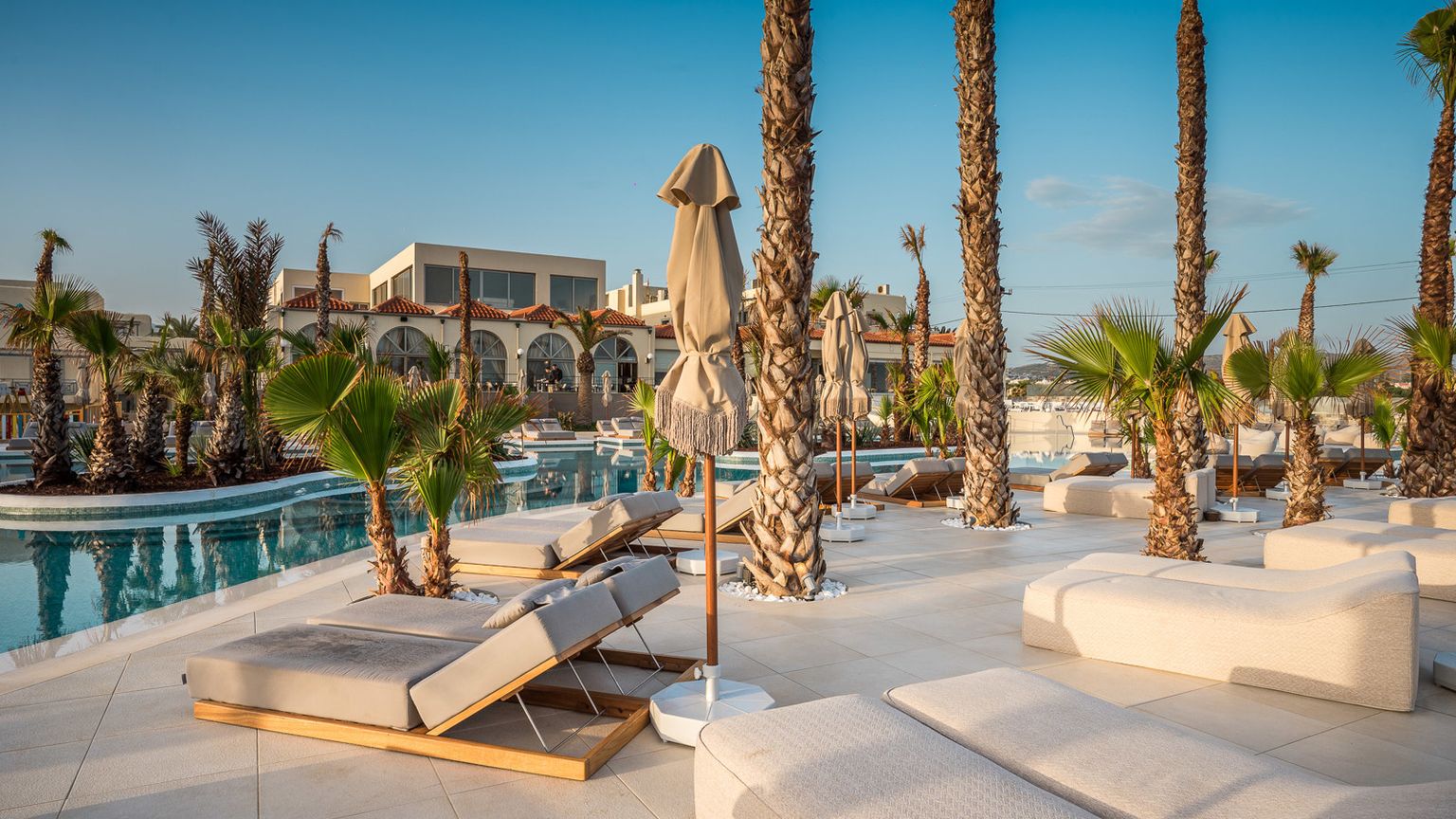Zona de piscina soleada en un resort con palmeras, tumbonas modernas y edificios del hotel. Stella Blue Seaside Resort