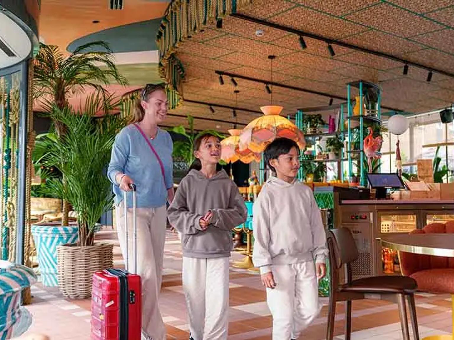 en kvinna och två barn går genom en hotellobby med en resväska.