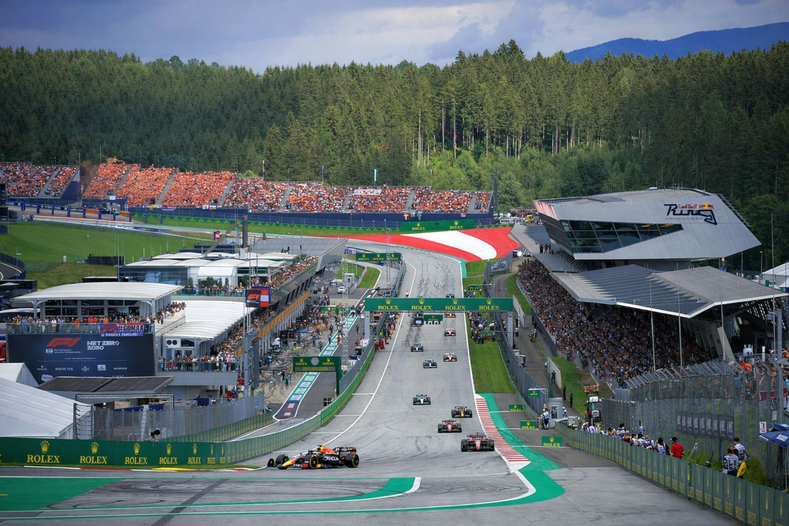 Formula 1 race at the Red Bull Ring with cars on track and spectators in the grandstands.