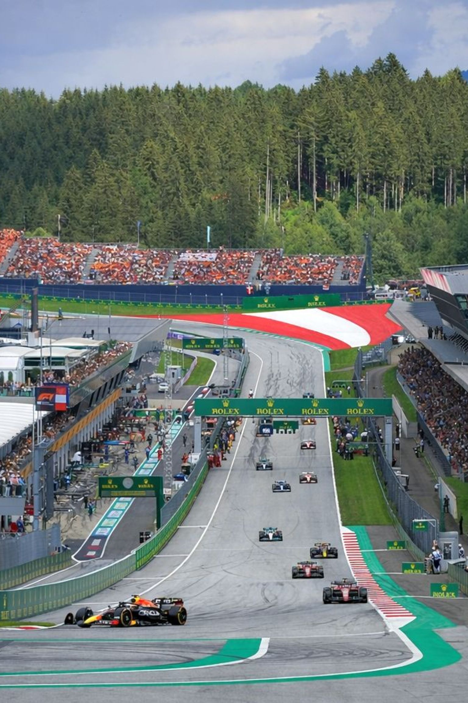 Formula 1 race at the Red Bull Ring with cars on track and spectators in the grandstands.