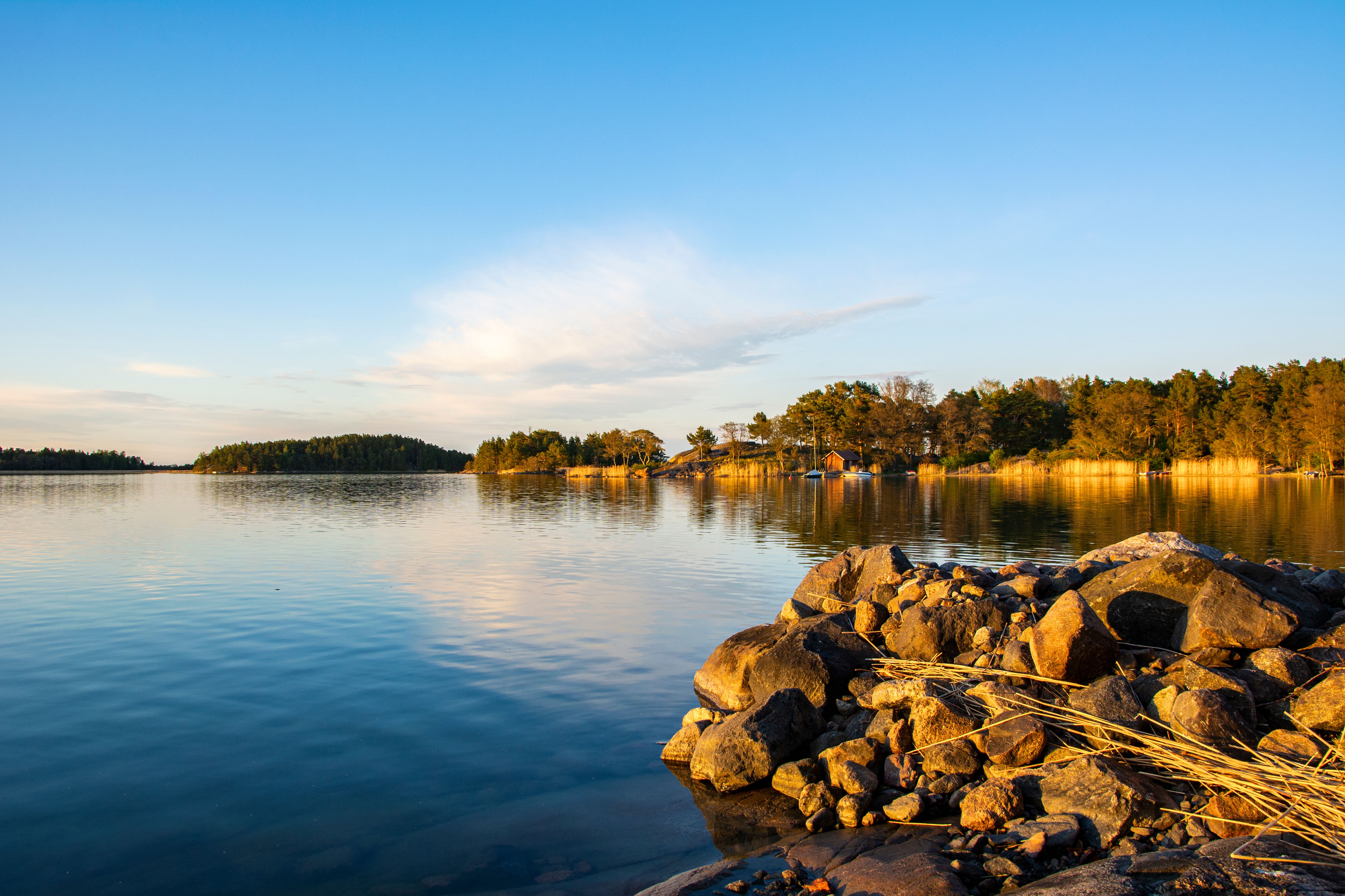 Gyldentimeslys over roligt vand, klippefyldt forgrund og træklædte øer.
