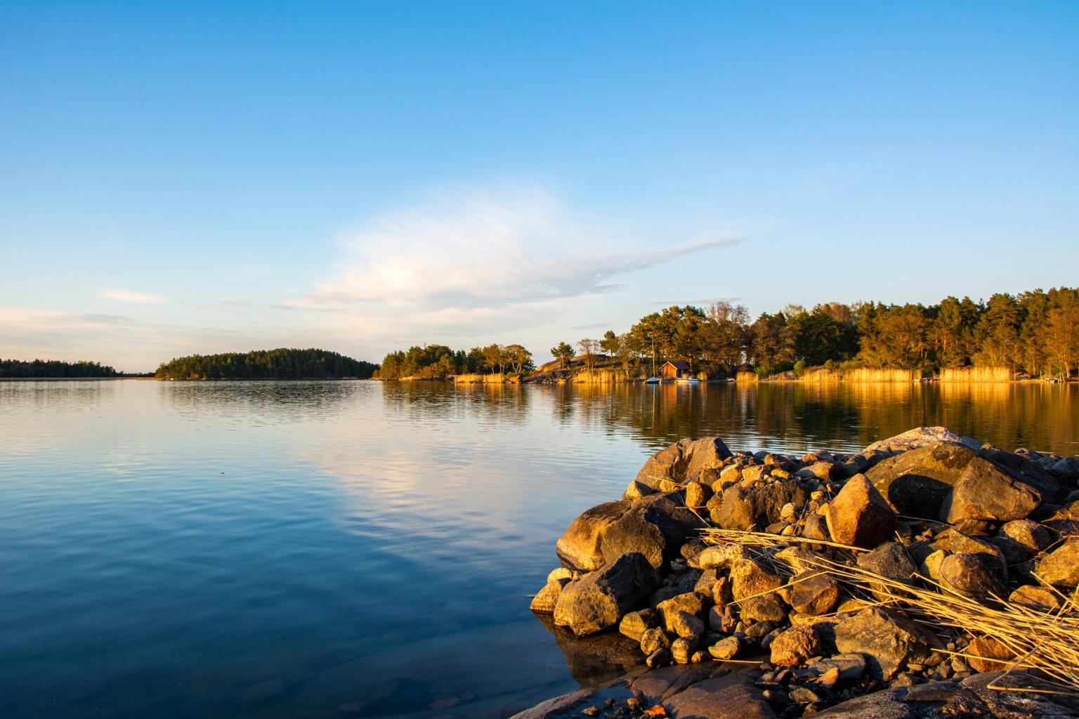 Gyldentimeslys over roligt vand, klippefyldt forgrund og træklædte øer.