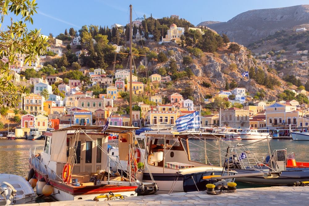 Boats docked in a harbor with colorful houses climbing a steep hillside. Symi, Greece