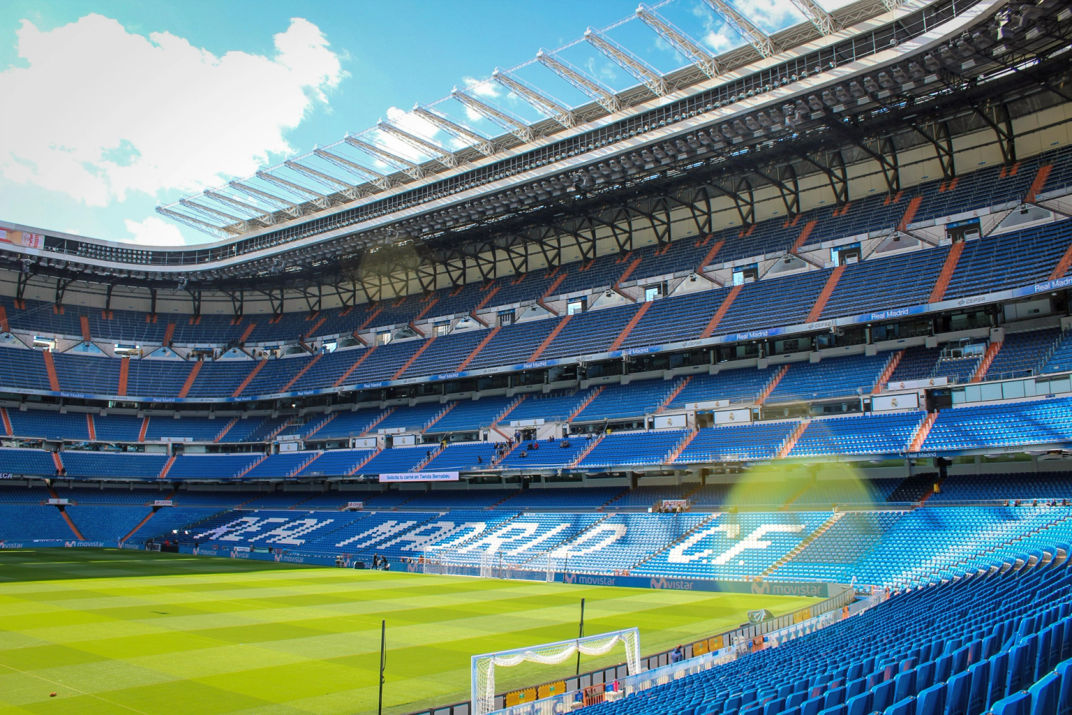 Leeres Real Madrid C.F. Fußballstadion mit blauen Sitzen und einem grünen Spielfeld unter blauem Himmel.