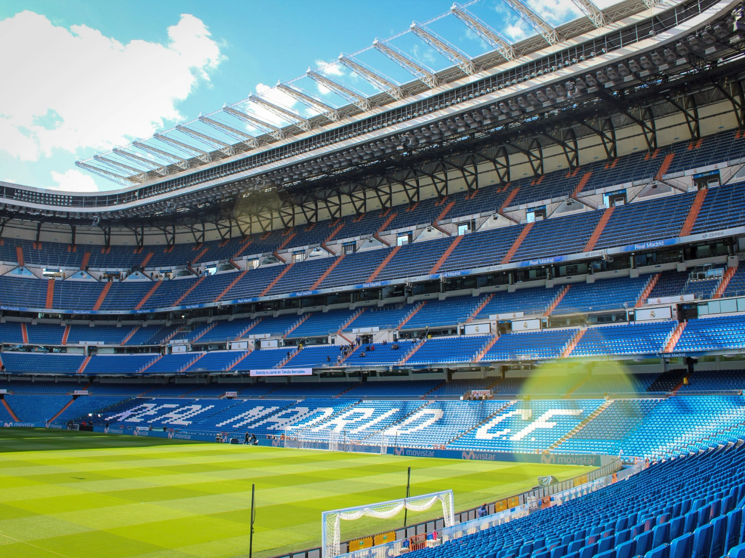 Üres Real Madrid C.F. futballstadion kék ülésekkel és zöld pályával kék ég alatt.