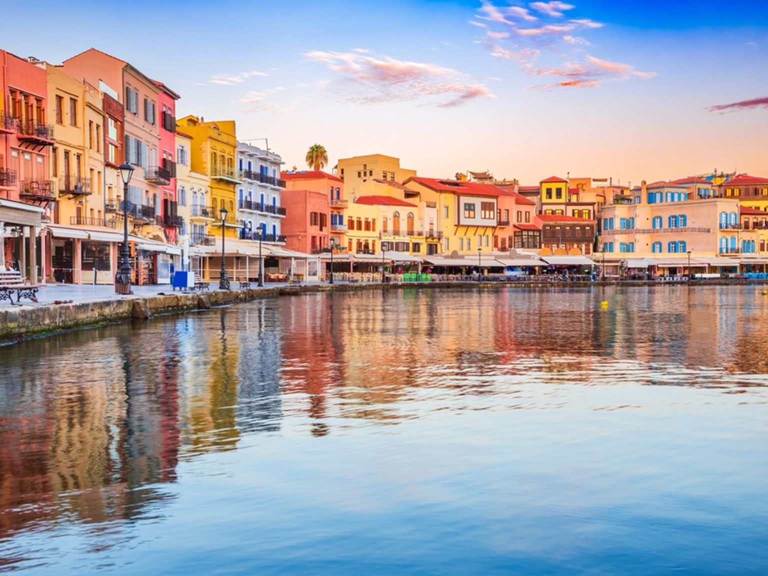 Farverige bygninger, der spejles i en rolig havn ved solnedgang.