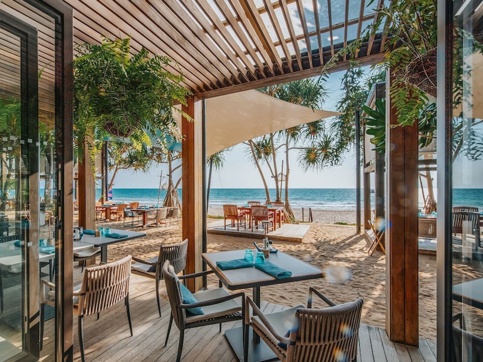 ein Restaurant am Strand mit Tischen und Stühlen und Blick auf das Meer.