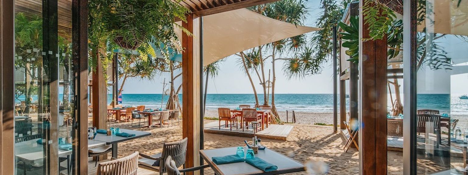 ein Restaurant am Strand mit Tischen und Stühlen und Blick auf das Meer.