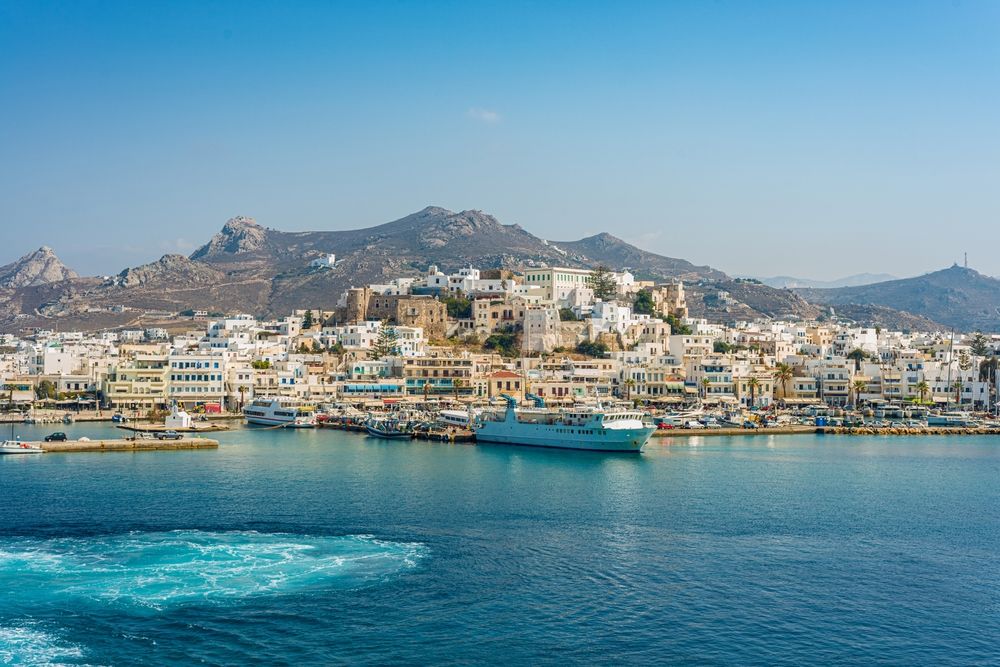 A white coastal town with a busy harbor and mountains in the background. Paros, Greece