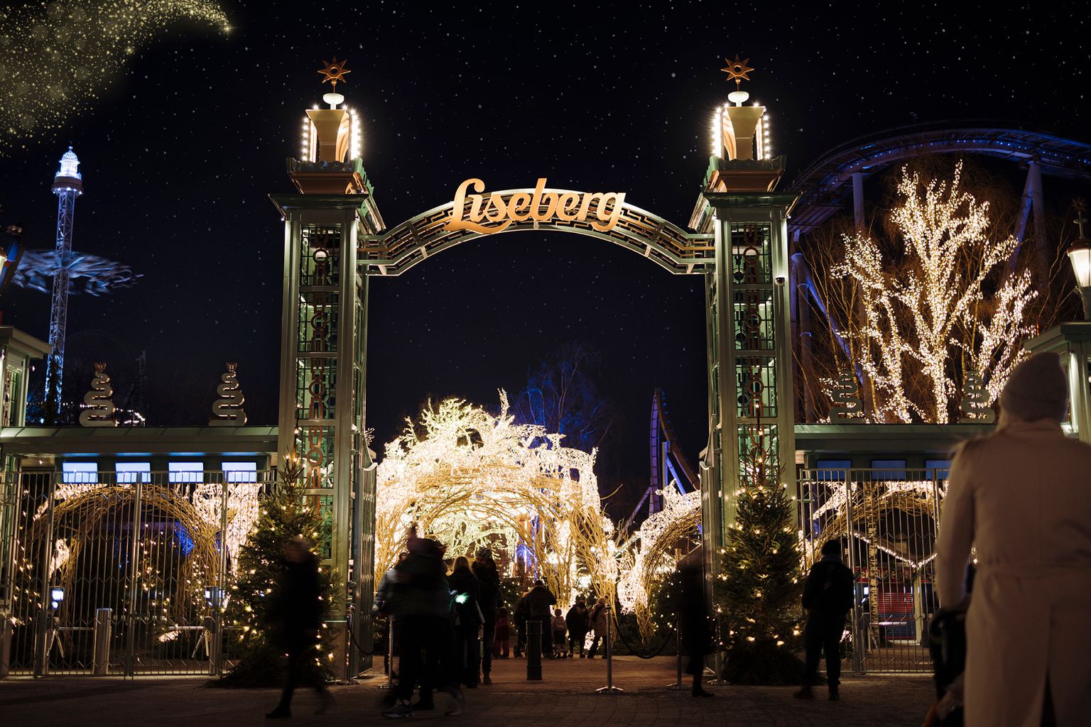 Liseberg forlystelsespark indgang om natten, lyst op med julelys, mens folk går ind.
