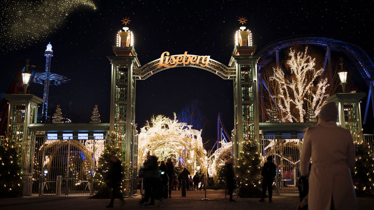 Liseberg forlystelsespark indgang om natten, lyst op med julelys, mens folk går ind.