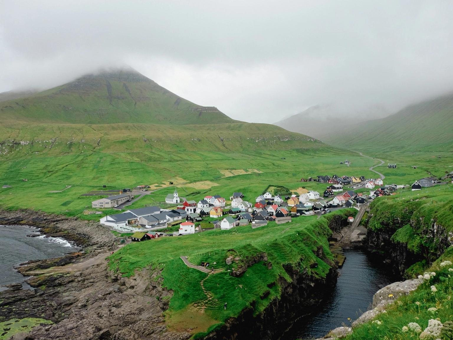 a small village on a hillside next to a river with a mountain in the background