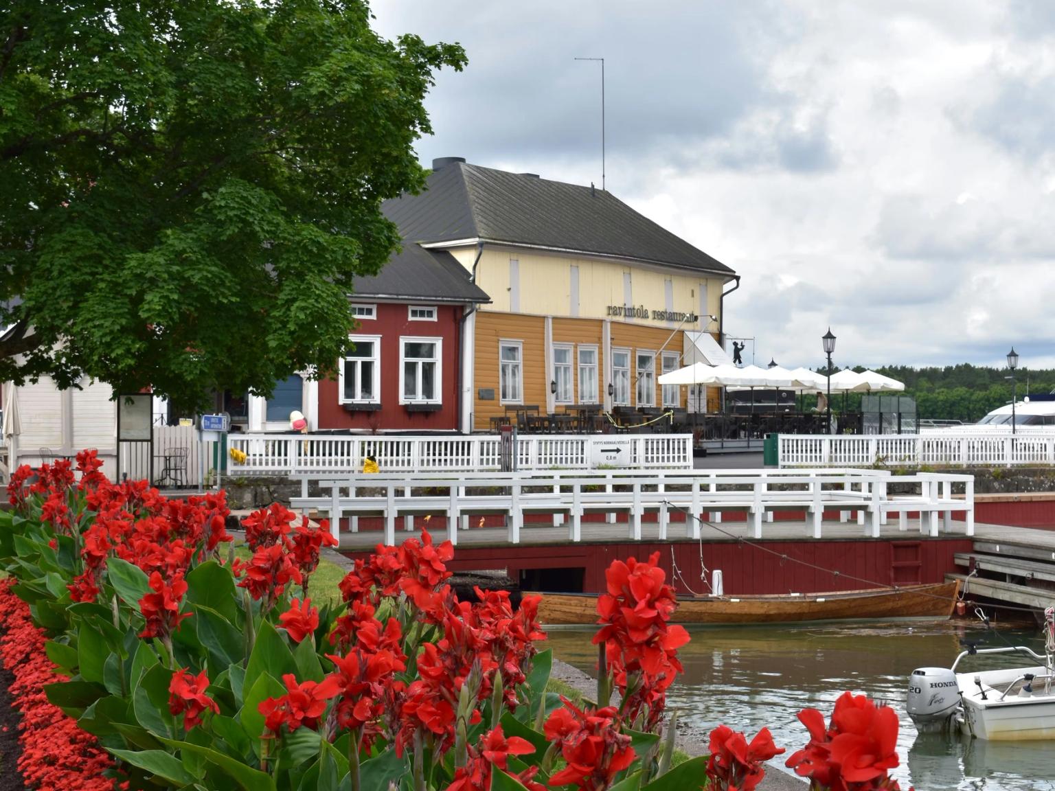 Røde blomster pryder en havnefront med farverige bygninger, både og en overskyet himmel.