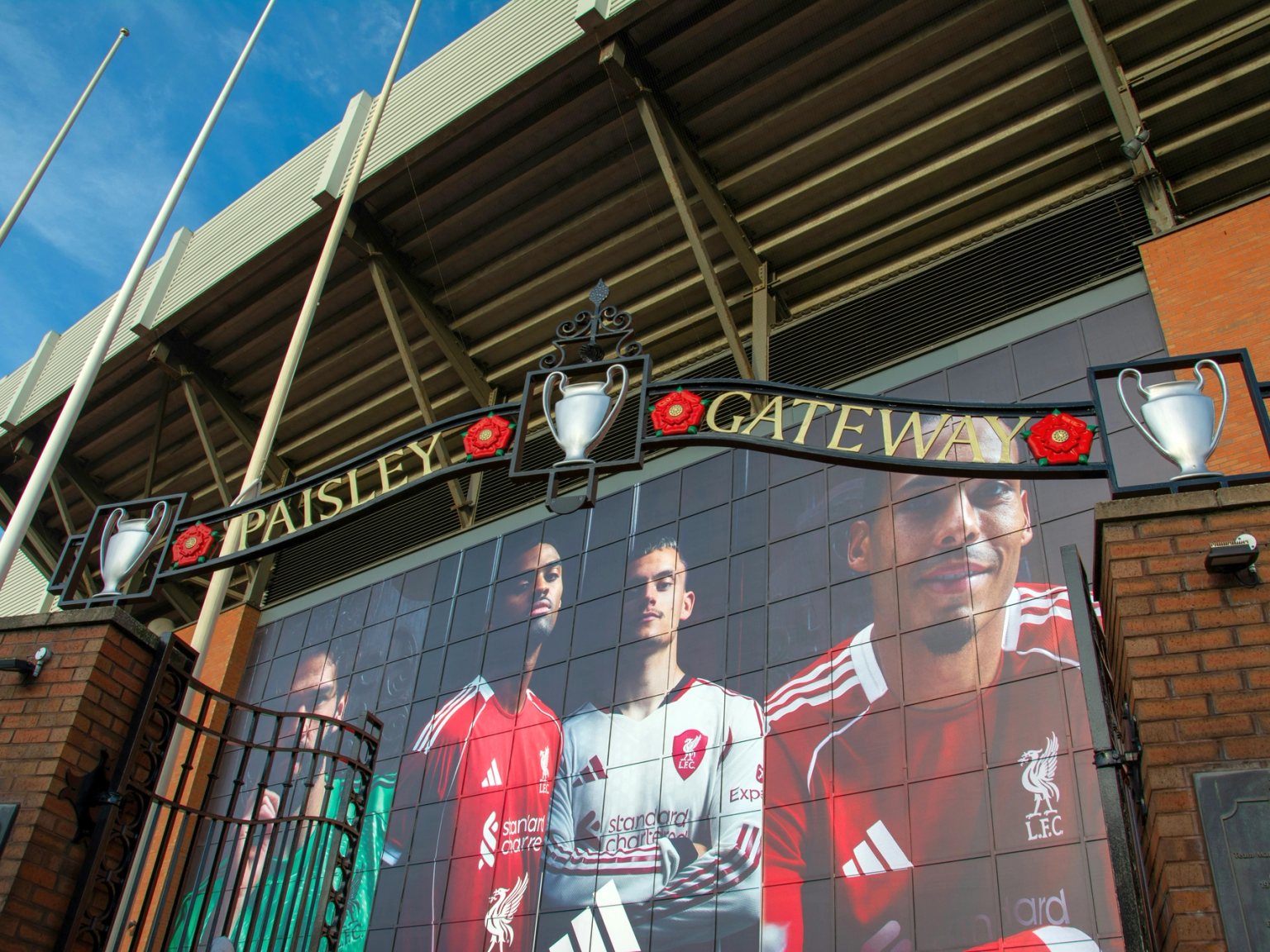 Paisley Gateway -kyltti, jossa on pokaaleja ja ruusuja Liverpool FC:n pelaajien seinämaalauksen yläpuolella stadionilla.