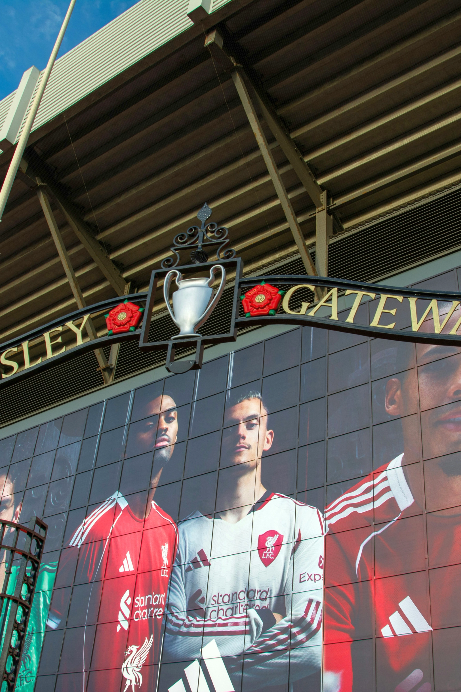 Paisley Gateway -kyltti, jossa on pokaaleja ja ruusuja Liverpool FC:n pelaajien seinämaalauksen yläpuolella stadionilla.