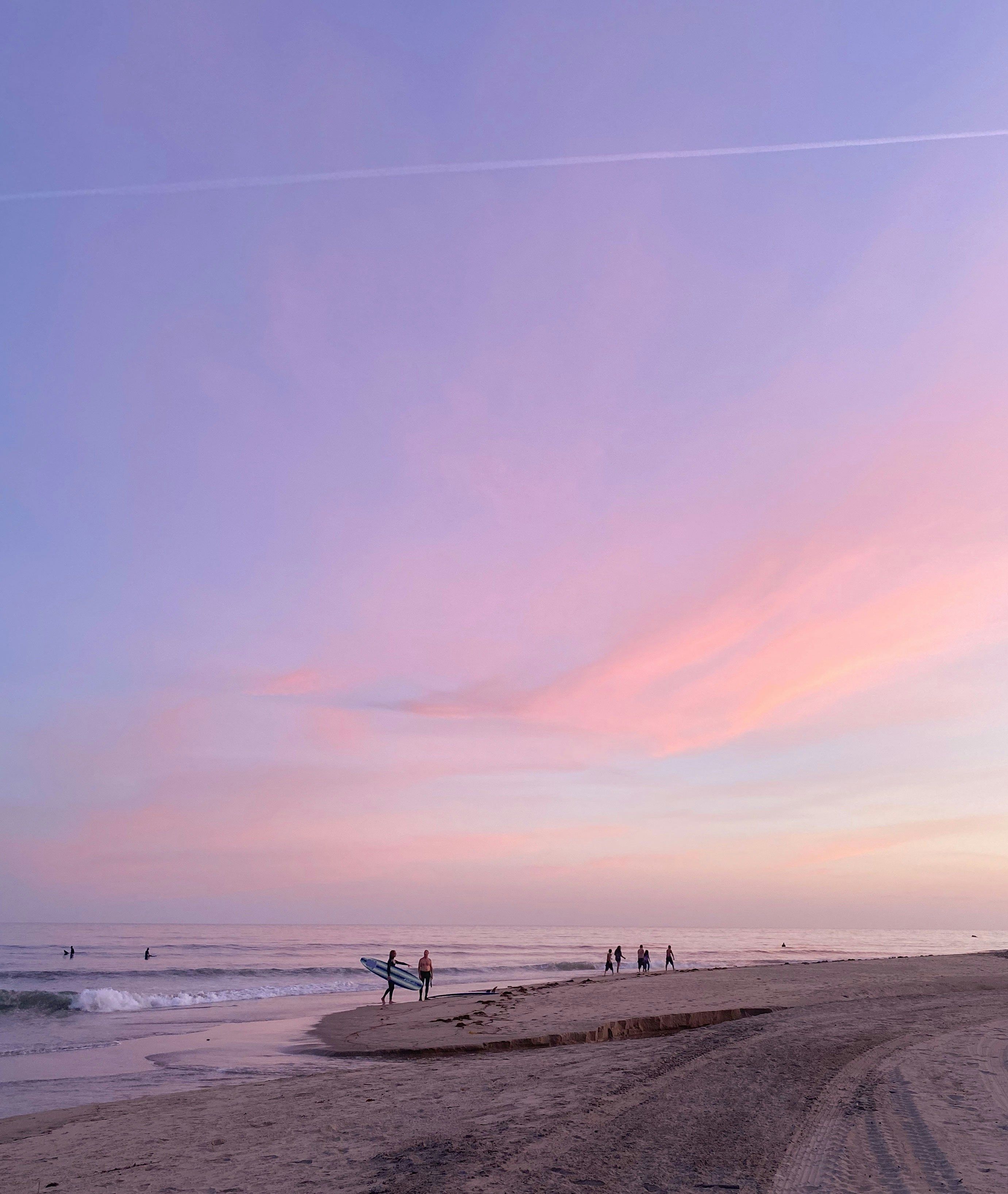 a group of people are standing on a beach at sunset.