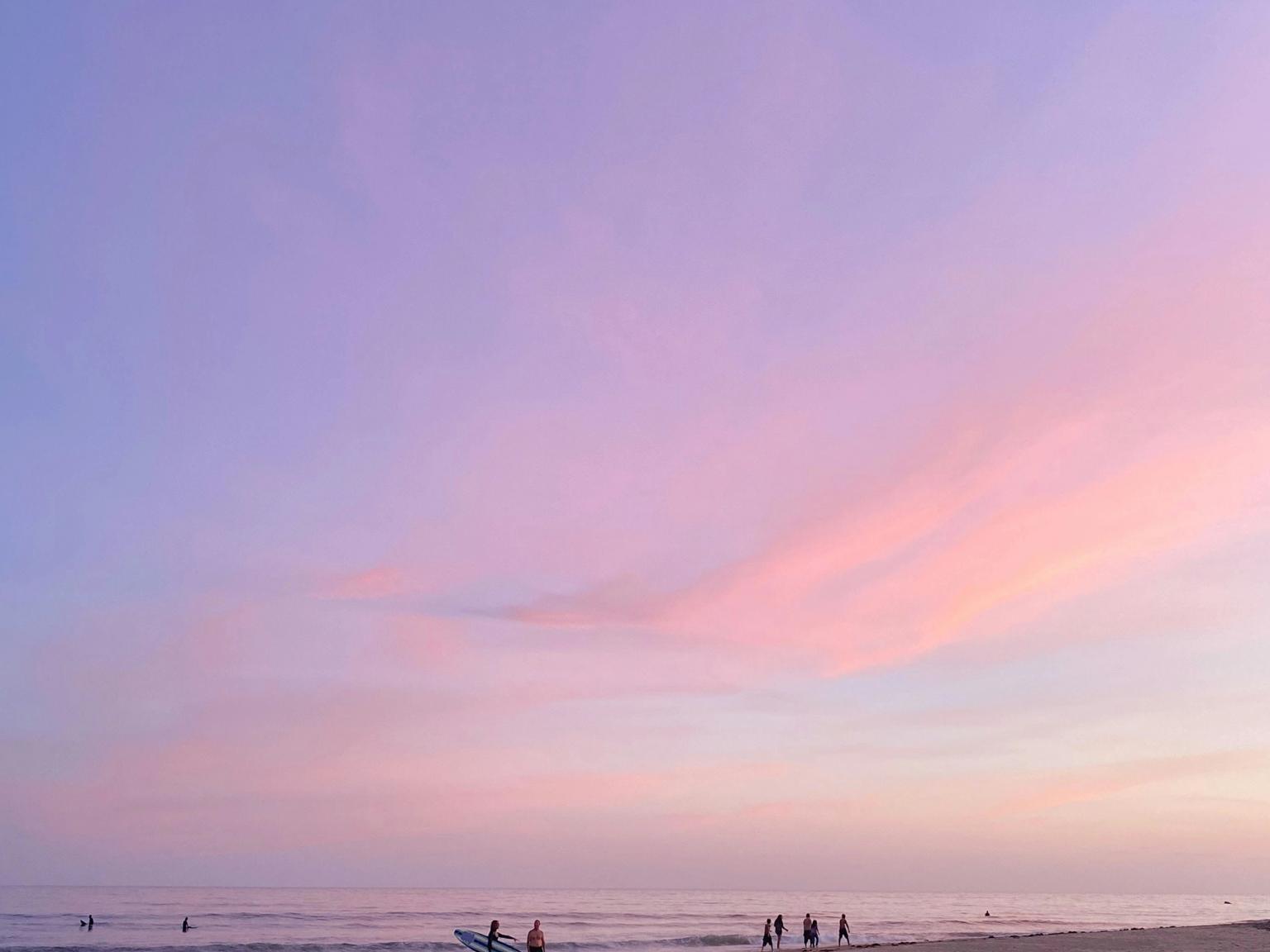 a group of people are standing on a beach at sunset.