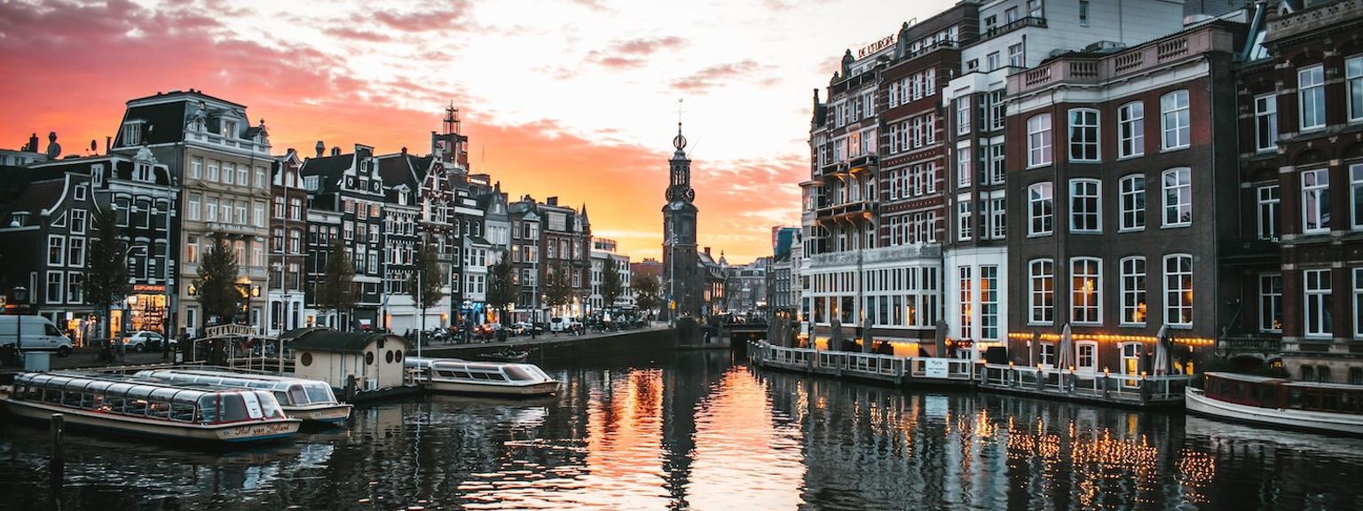 en kanal i Amsterdam med båtar och byggnader i bakgrunden vid solnedgången.