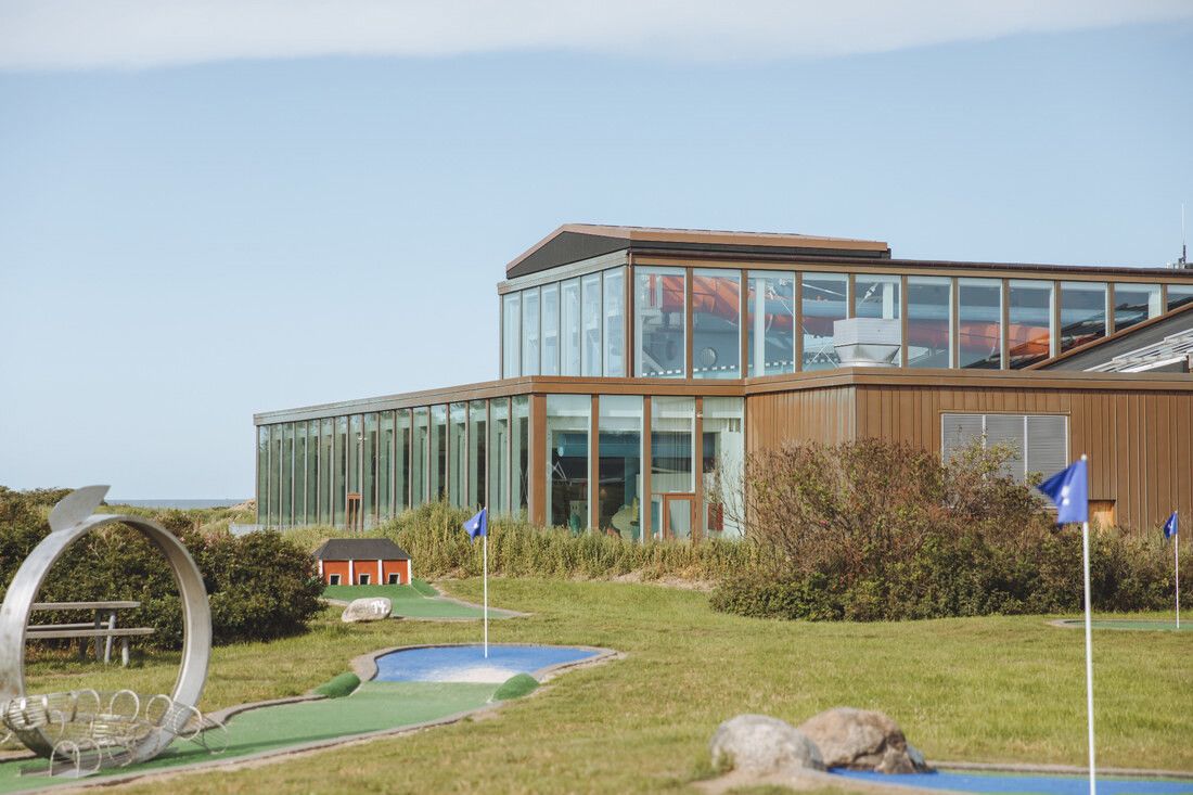En minigolfbana framför en modern byggnad med stora fönster under en klar himmel.