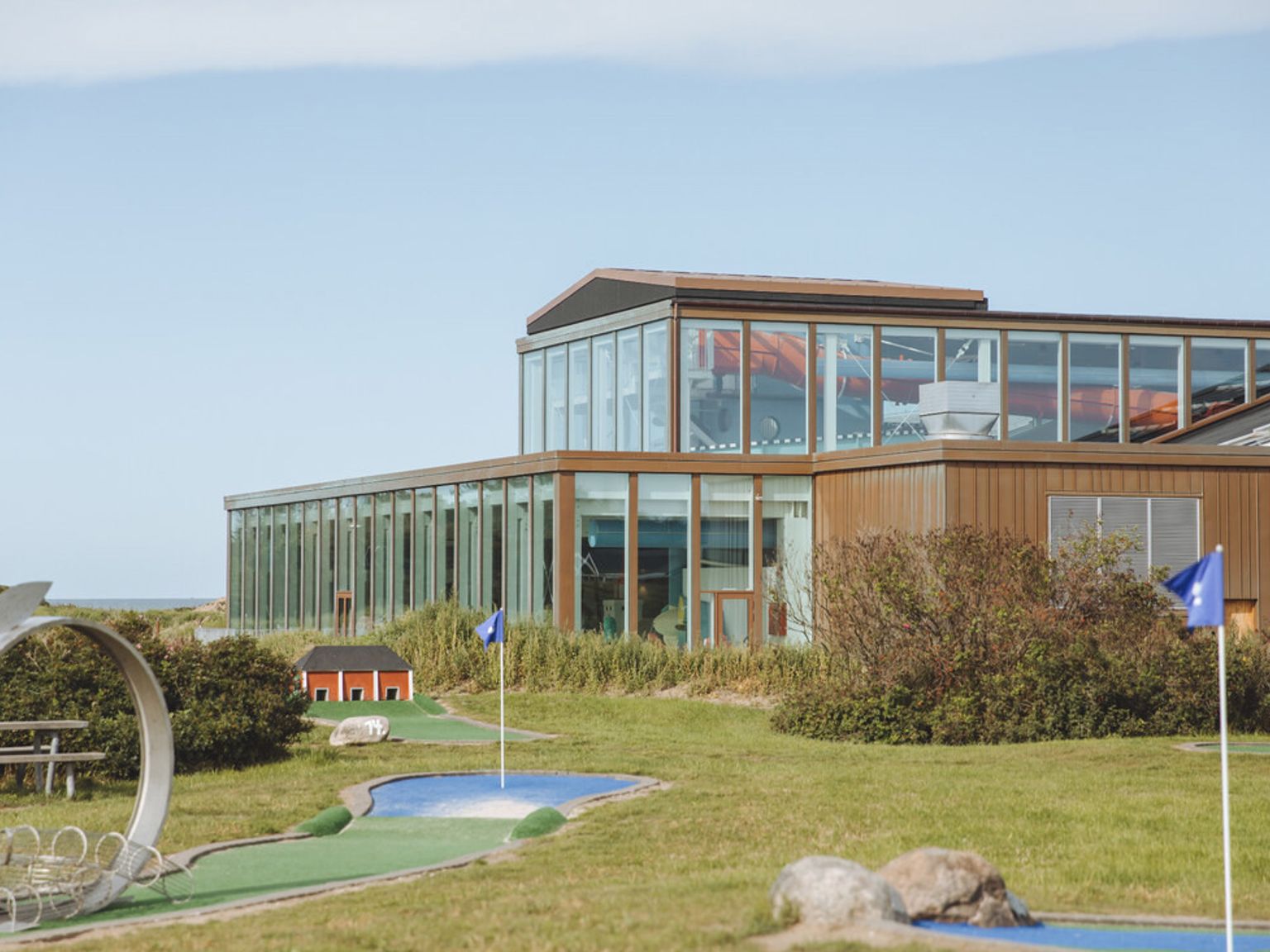 En minigolfbane foran en moderne bygning med store vinduer under en klar himmel.
