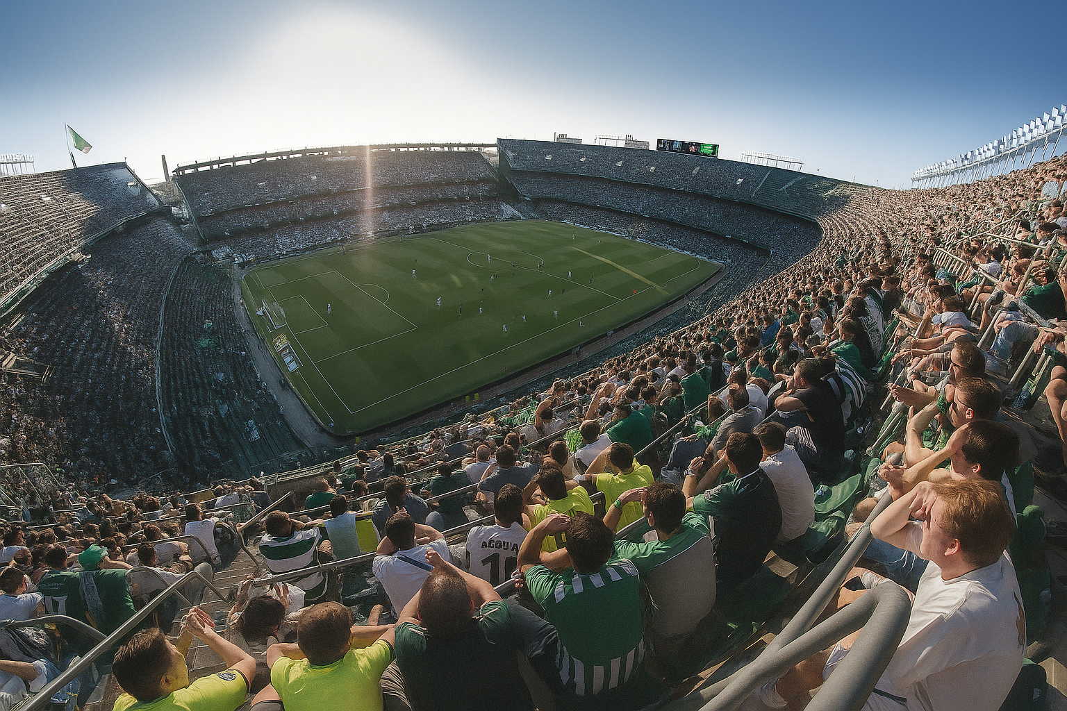 Wide-angle view of a soccer stadium packed with fans in green and white under bright sun.