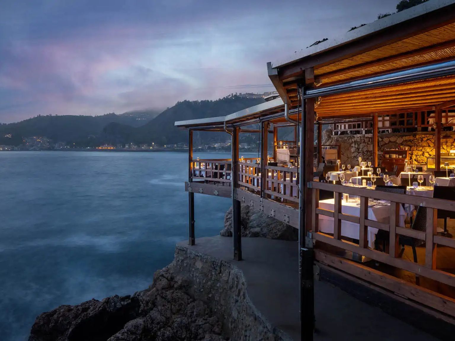 en restaurang på en klippa med utsikt över havet med bord och stolar, UNAHotels Hotel Capotaormina