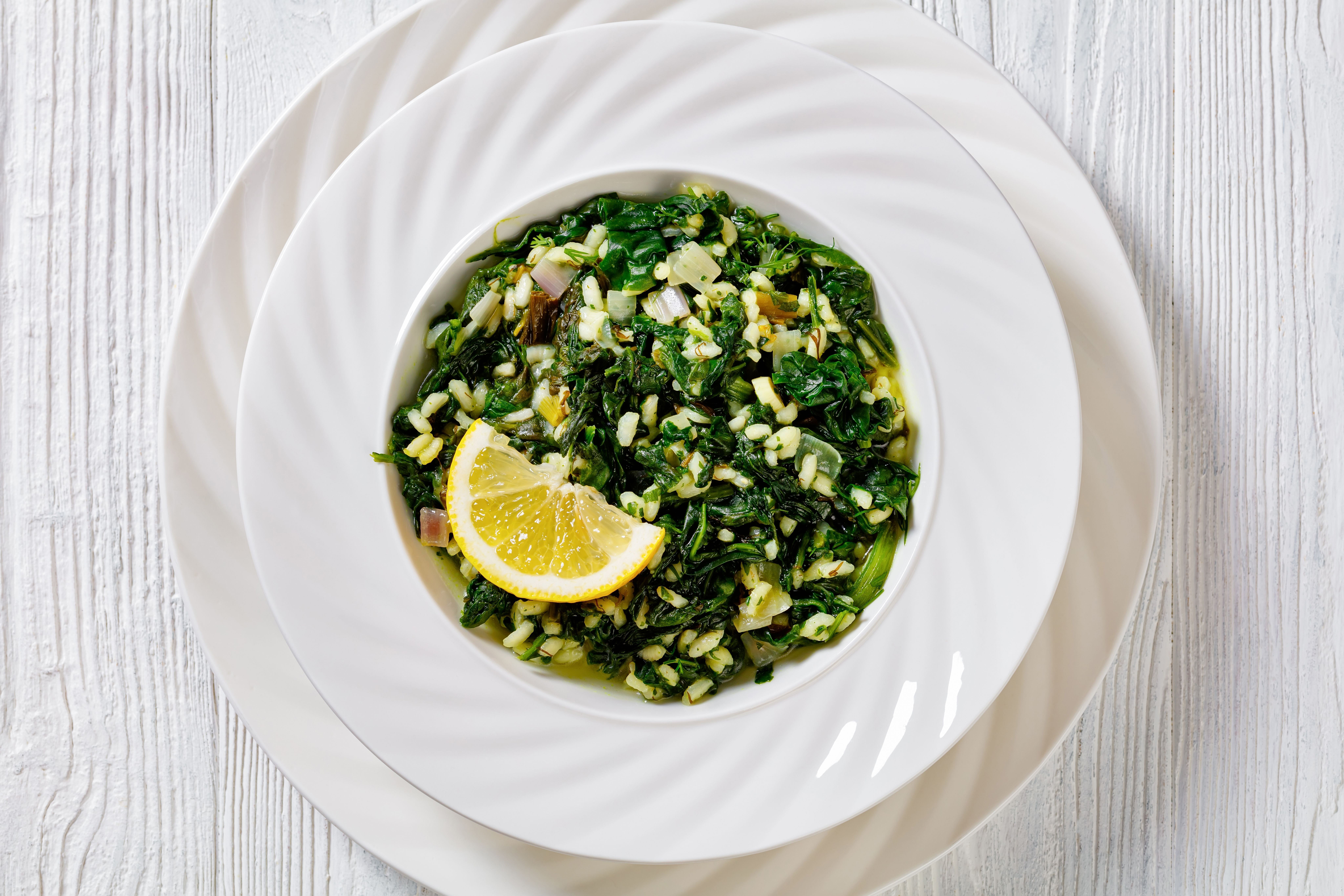 a bowl of spinach and rice with a slice of lemon on a plate