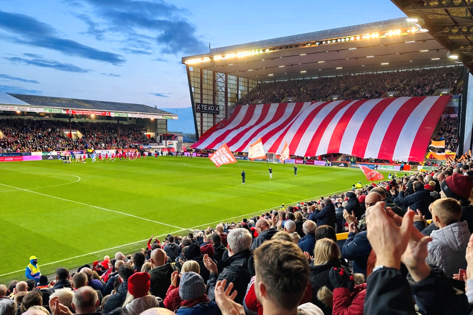 A packed football stadium with a giant red and white striped banner across the stands.