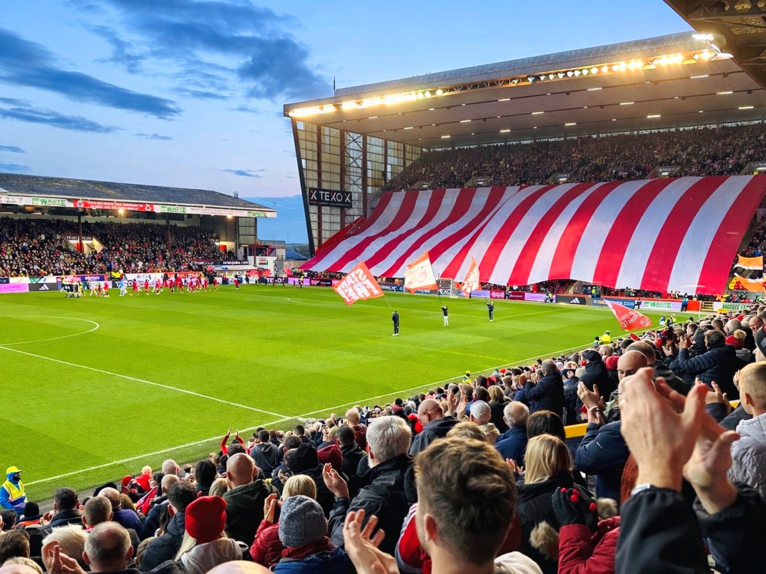 Et fyldt fodboldstadion med et kæmpe rødt og hvidt stribet banner over tribunerne.